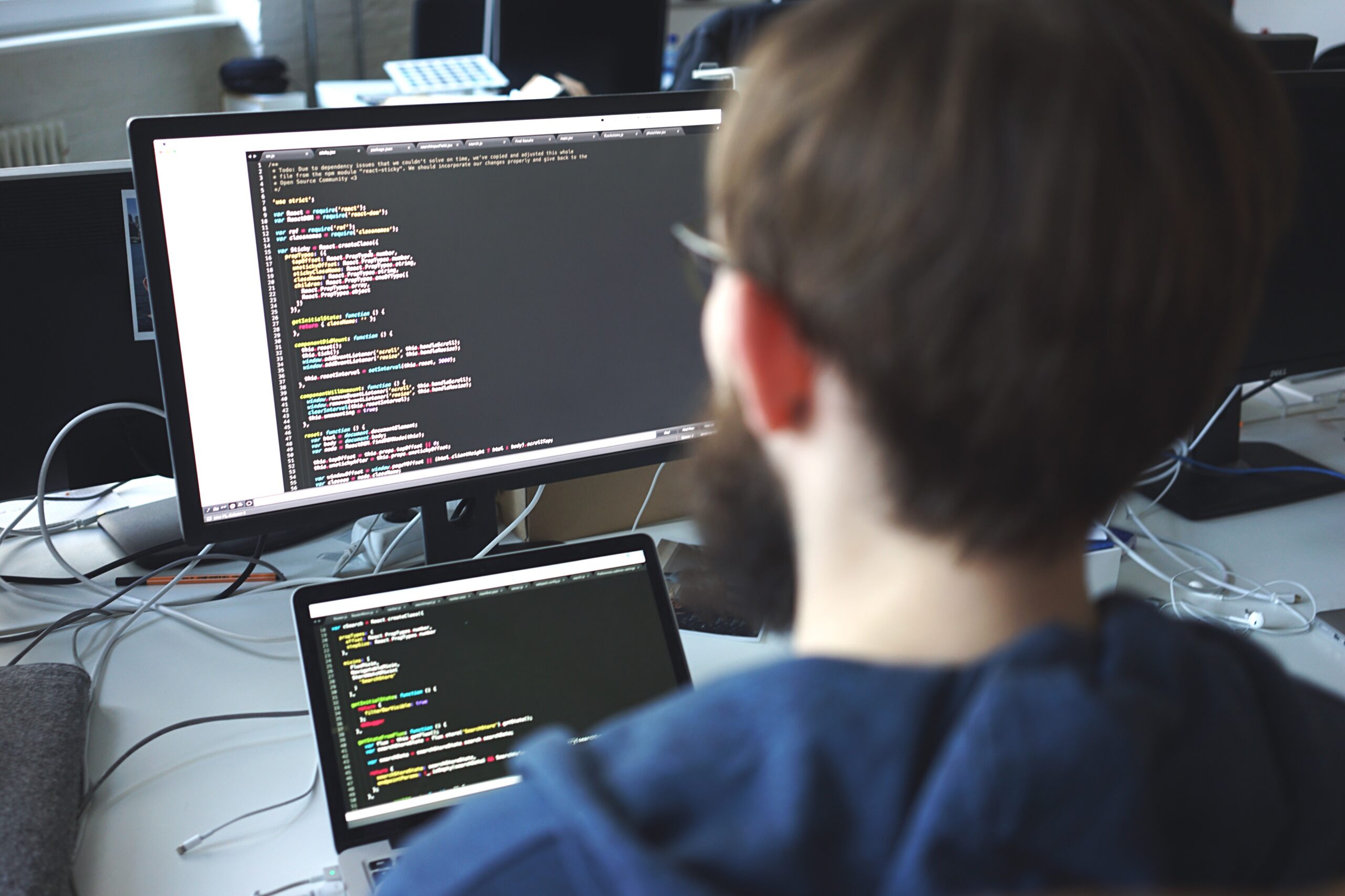Sviluppatore al lavoro su codice software visualizzato su due monitor in ambiente di sviluppo backend.