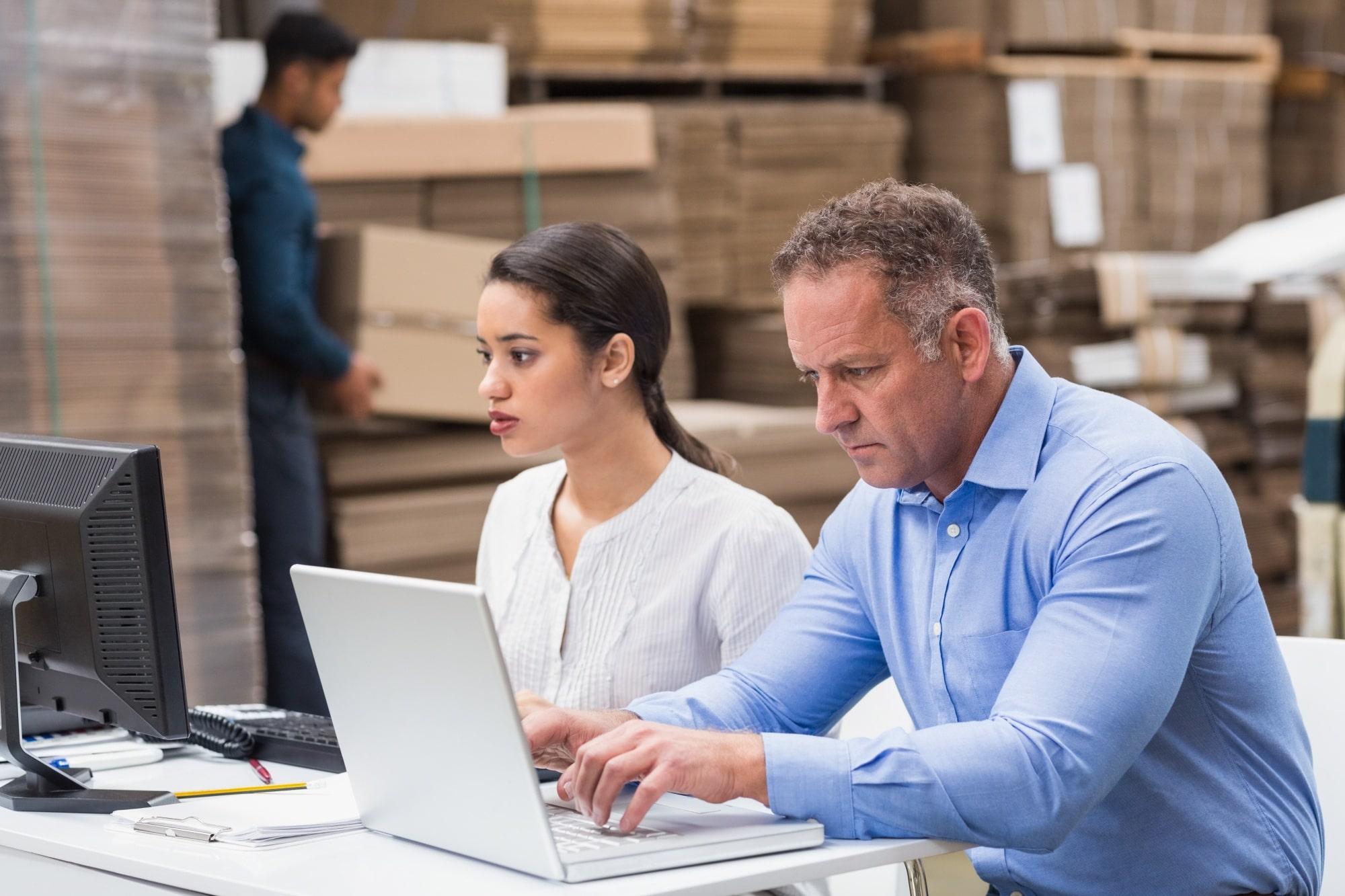 dati sempre aggiornati con le applicazioni enterprise: due lavoratori lavorano al pc da un magazzino logistico